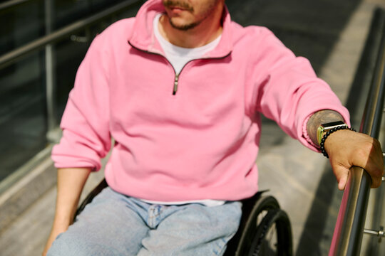 Male in wheelchair holds metal handrail on urban ramp outdoors