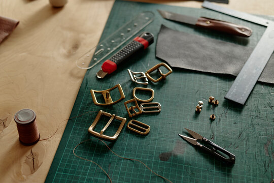 Leatherworking tools and brass buckles lie on a workshop table