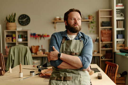 Confident artisan man stands thinking in his indoor craft workshop