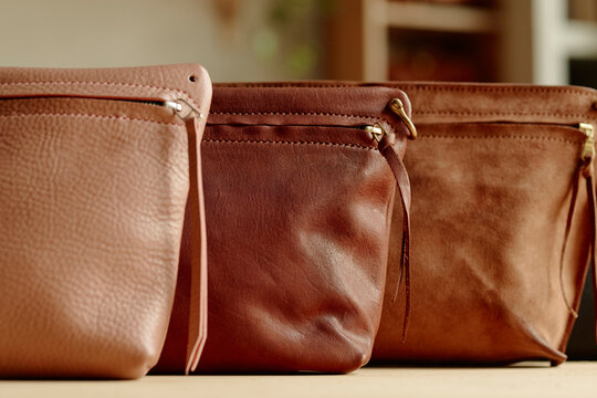 Three handmade genuine leather bags sit on a workshop table