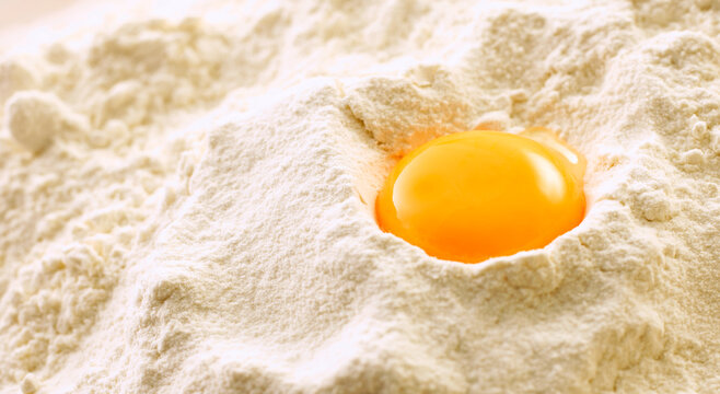 Raw egg yolk sits in a mound of white flour for baking preparation