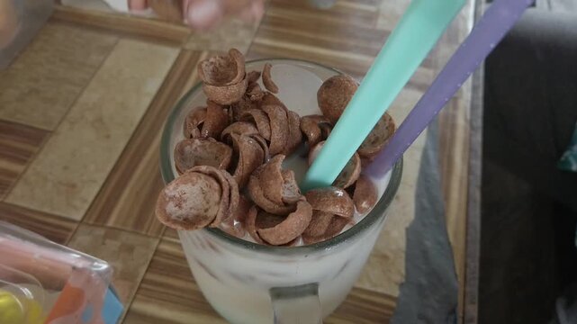 A person drinking a mixture of creamer and chocolate cereal from a glass, showing a simple homemade beverage preparation and consumption activity.