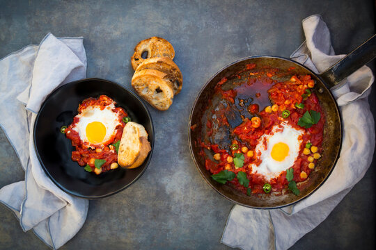 Shakshouka with chick peas in pan and slices of roasted baguette