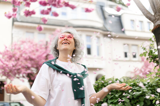 Smiling mature woman catching cherry blossom petal on city street