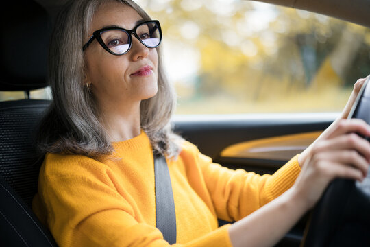 Confident woman with grey hair drives a car in autumn