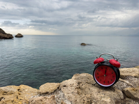 Retro red alarm clock on rocks overlooking the sea