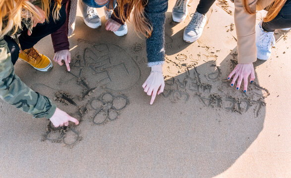 Four friends drawing in the wet sand on the beach, partial view