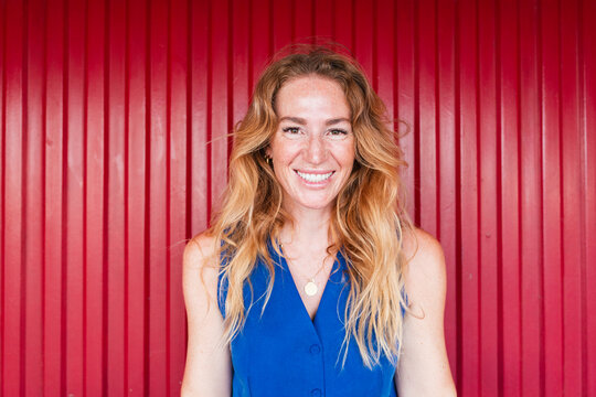 A smiling woman wears a blue vest against a red corrugated wall