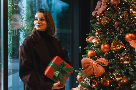 Smiling woman with wrapped gift near decorated Christmas tree