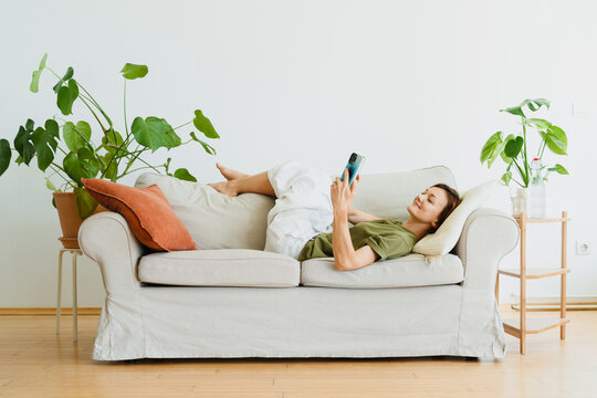 Relaxed woman uses her smartphone on a sofa at home