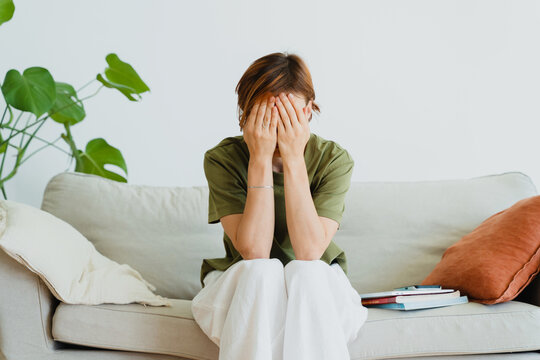 Sad woman covering face while sitting on sofa indoors