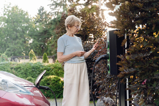Woman uses smartphone while charging electric car outdoors