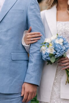Bride holding blue bouquet embracing groom arm.