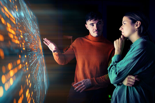 Man and woman analyzing data on a large digital screen in the office