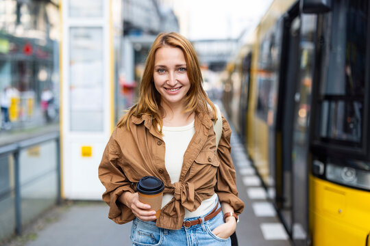 Smiling woman holds coffee while waiting for the tram in Berlin