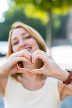 Smiling woman makes heart shaped hands outdoors in Berlin