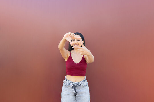 Smiling woman makes a hand frame against a brown background