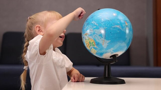 Little blonde girl spinning globe model and exploring world map at home