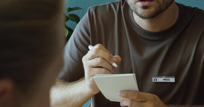 Press officer taking notes while speaking with another person during a professional media conversation.