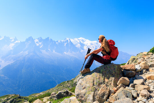 Female hiker with backpack sitting on rock looking at Mont Blanc snowy mountains landscape- adventure, freedom, wanderlust concept