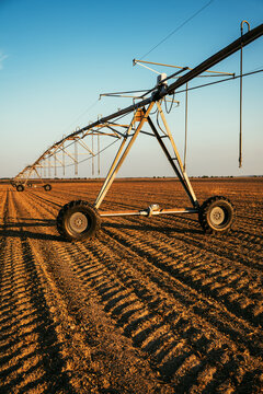 Agricultural irrigation machinery standing over tilled farmland under a clear afternoon sky. Concept of smart farming, water management, agricultural technology, and crop production.