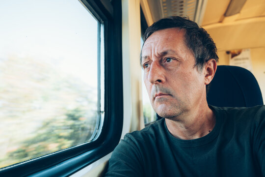 Pensive man commuting by train looking out the window as scenery blurs past. Concept of travel, quiet reflection, passenger journeys, and public transportation.