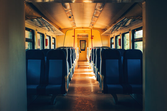 Sunlit interior of a passenger railway carriage with empty seats arranged along a central aisle. Train travel, public transportation, commuting, journey and railway tourism concept.
