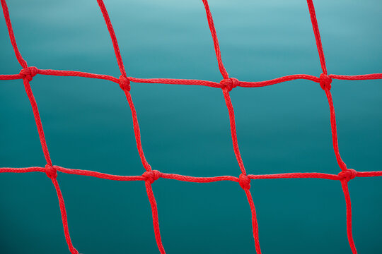 Close-up of a red water polo goal net showing knot details against a deep blue water background.