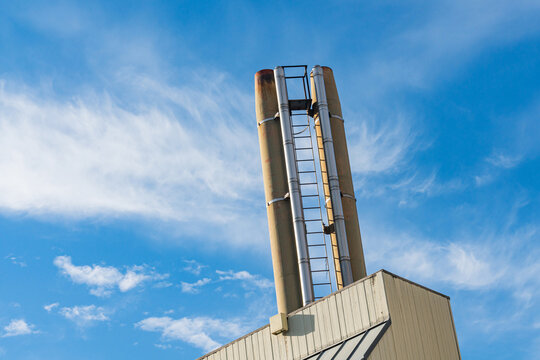 Two tall industrial chimneys under a blue sky with clouds