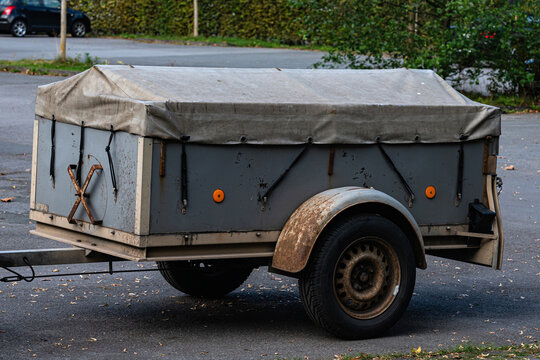 Small trailer with a gray cover parked in a lot near green bushes