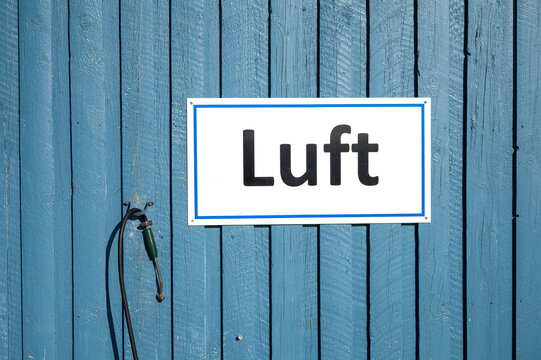 Blau gestrichene Holzwand mit wei&szlig;em &bdquo;Luft&ldquo;-Hinweisschild und Fahrradpumpe, aufgenommen bei hellem Tageslicht mit maritimer, klarer Farbwirkung.