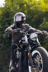 Obraz premium Biker wearing full-face helmet and leather jacket riding a vintage style motorcycle, looking forward on an outdoor adventure