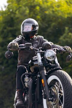 Biker wearing full-face helmet and leather jacket riding a vintage style motorcycle, looking forward on an outdoor adventure