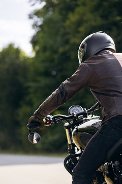 Person wearing leather jacket and helmet riding a classic motorcycle, traveling on an open road through nature