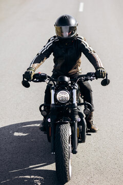 Person wearing leather jacket and helmet riding a classic black motorcycle on an asphalt road, embracing travel and adventure