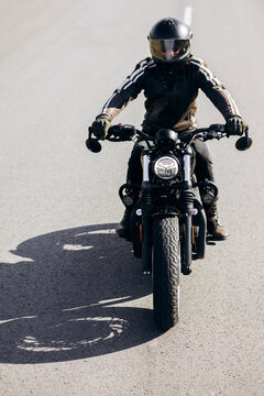 Biker wearing a black helmet and leather jacket riding a motorcycle on a paved road, representing travel and adventure