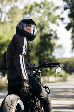 Biker wearing a helmet and leather jacket, sitting on a motorcycle on an open road, looking to the side