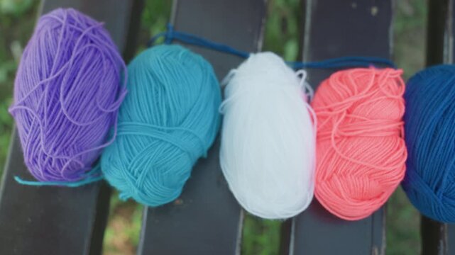Close up of hand rearranging colorful yarn balls on outdoor bench. scene features purple blue red white pink and dark blue skeins arranged in sequence with soft natural lighting. Background