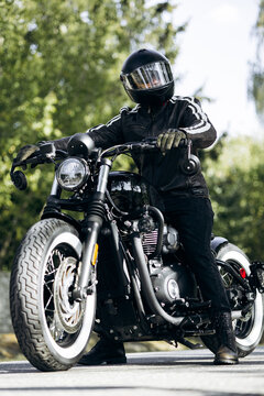 Motorcycle rider in a black helmet and leather jacket stopping on a road, ready for the next part of his journey