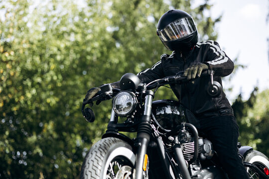 Biker in black leather jacket and helmet cruising a classic custom motorcycle on an open road trip, vintage style and freedom