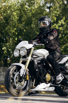 Motorcyclist wearing full protective gear, black helmet, jacket, and gloves, sitting on a white naked sportbike