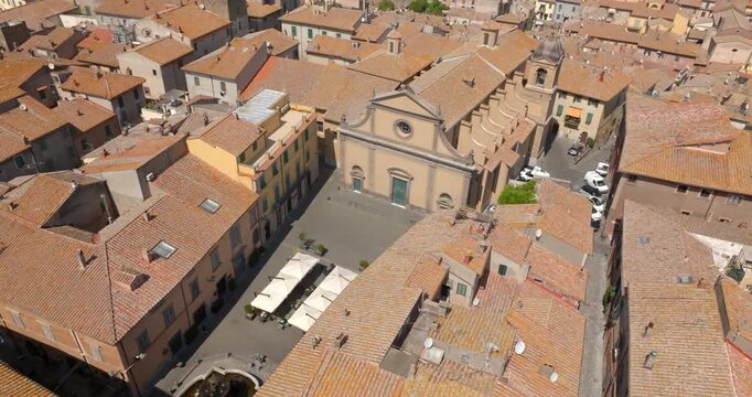 Aerial view of a church with a pediment facade, rose window and bell tower on a square in the historic center of Tuscania, in the province of Viterbo, in Lazio, Italy, among tiled roofs on a sunny day