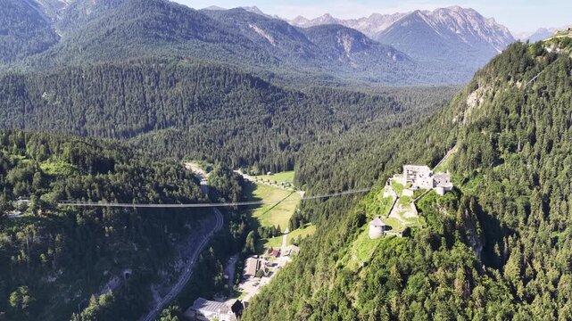 Ehrenberg castle and suspension bridge span forested mountain valley near Reutte, Austria, aerial drone shot of ruins, turrets and Tirol Alps.