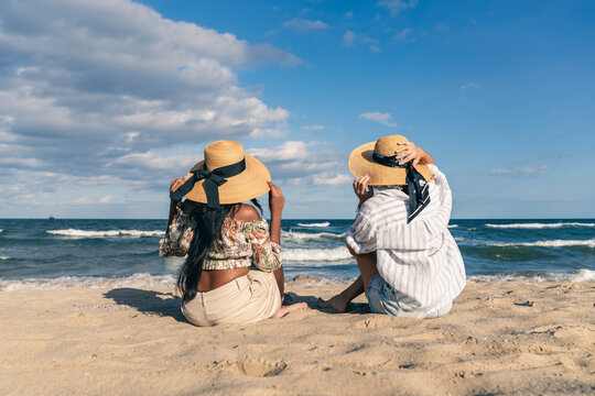 Senior and young woman holding their hats on a windy beach