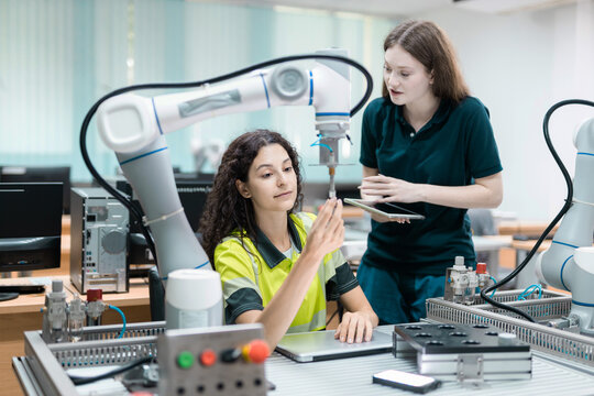 Engaged young woman student engineer in teamwork, learning about robot technology with robotic arm. Future education for industry automation and modern programming for machinery