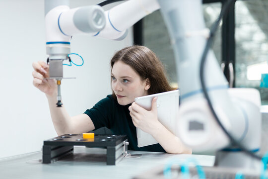 Female engineer closely inspecting and adjusting robotic arm components in high-tech industrial environment, symbolizing precision, innovation, smart automation.
