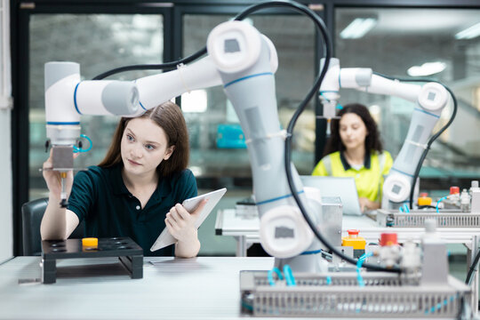 Engaged young woman student engineer in teamwork, learning about robot technology with robotic arm. Future education for industry automation and modern programming for machinery