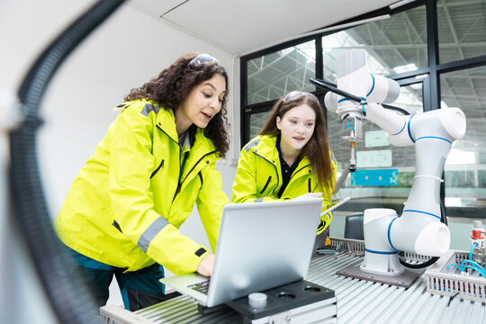 Engaged young woman student engineer in teamwork, learning about robot technology with robotic arm. Future education for industry automation and modern programming for machinery