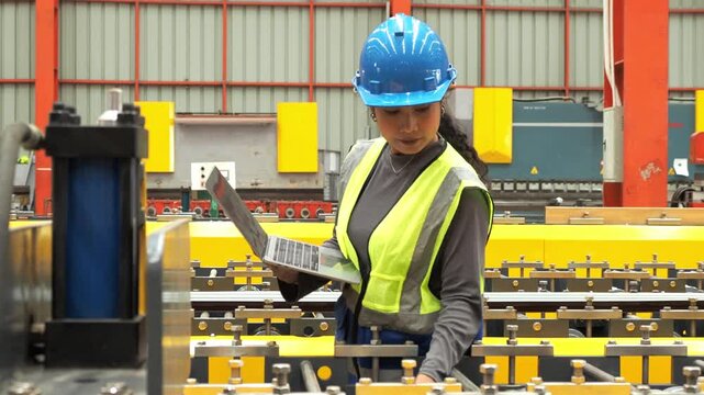 Female Engineer Inspect Automated Factory Machinery With Laptop : Professional Asian female technician hardhat check industrial roll forming line use laptop computer in manufacturing plant.