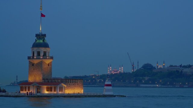 A breathtaking evening view of the historic Maiden's Tower illuminated on the Bosphorus strait with the iconic silhouette of Hagia Sophia and mosques in Istanbul